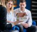 Close up shot of female realtor, interior designer hands showing 3d model of house to cute caucasian couple on the blue modern office background.
