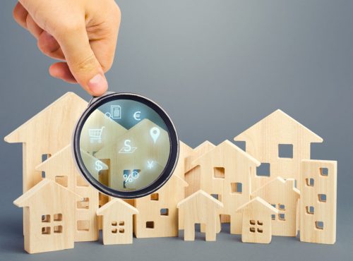 Realtor examines houses through a magnifying glass. Review of the real estate market, search for the best offers based on the criteria of price, location, area, infrastructure. Customer preferences.